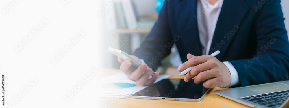 Poster businessman uses phone and a stylus on tablet at desk with a laptop and copy space , modern remote w