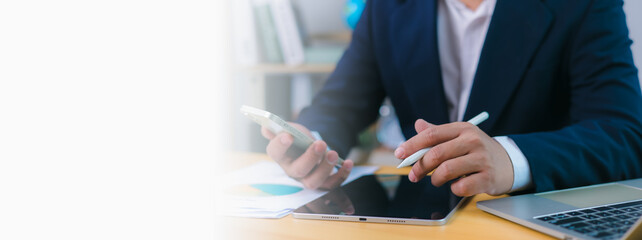 Businessman uses phone and a stylus on tablet at desk with a laptop and copy space , Modern remote work, digital productivity, technology integration, Efficient multitasking in a professional setting.