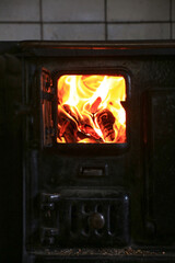 View of old stove with tiled wall and glowing fire visible through small front-facing window