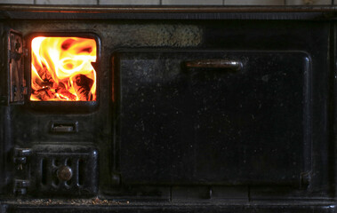 Full view of cast iron stove with fire glowing in left chamber and closed compartment on right