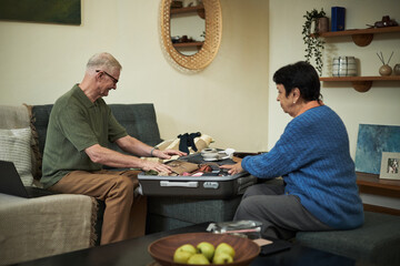 Senior man and woman packing a suitcase on a sofa in the living room, preparing for a trip. Various travel essentials are spread out in preparation for the journey