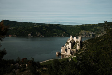 Elevated view of Golubac Fortress on the Danube, surrounded by lush green hills and blue sky. A popular tourist destination