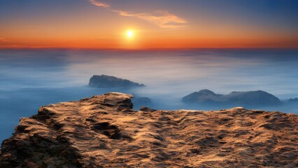 Obraz premium Beautiful sunset over the ocean, casting orange and blue hues across the sky and water, seen from a rocky beach