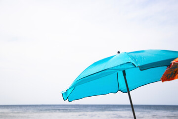 A blue beach umbrella stands on the sandy shore by the sea, offering shade under the warm sun on a...