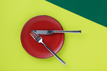 Plate and cutlery on green background, top view
