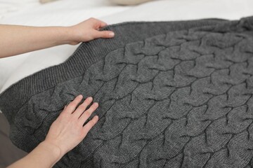 Woman putting woolen blanket on bed indoors, closeup