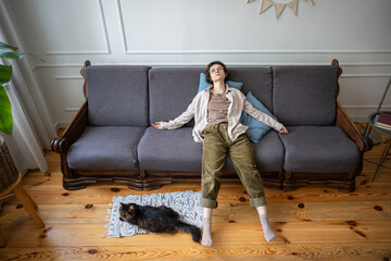 Woman lying still in apathetic pose, trapped in thoughts, with symptoms of domestic regression and emotional numbness. Feline companion nearby, silent coexistence, unable to get up, mentally stuck
