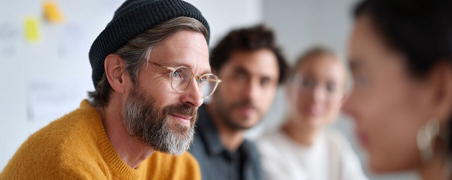 Focused man in beanie at a business meeting. Teamwork and collaboration represented. Corporate innovation or strategy themes. Diverse group concept. - Powered by Adobe