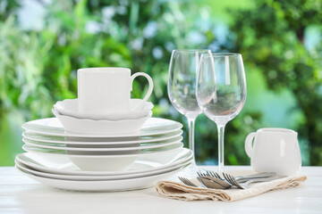 Different clean dishes on white table against blurred green background