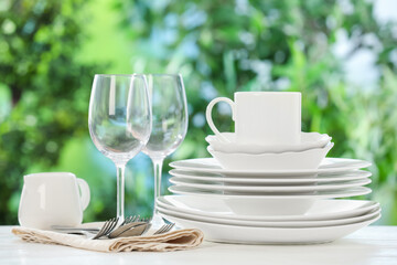 Different clean dishes on white table against blurred green background