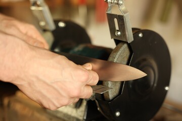 Man sharpening knife with bench grinder indoors, closeup