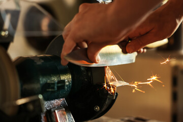 Man sharpening knife with bench grinder indoors, closeup