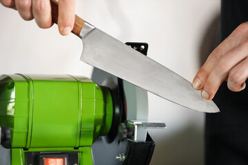 Man sharpening knife with bench grinder indoors, closeup