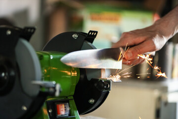 Man sharpening knife with bench grinder indoors, closeup