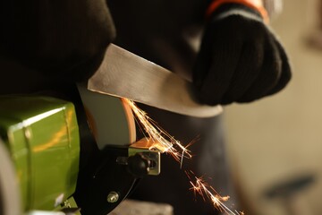 Man sharpening knife with bench grinder indoors, closeup