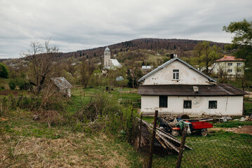 Fototapeta premium Spring landscape with a Christian church nestled among hills and forest. Tree branches frame the frame, creating a cozy, spiritual atmosphere