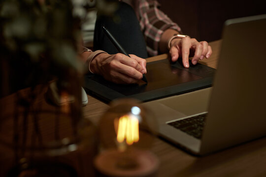female hands with graphic tablet retouching photo on laptop computer at night