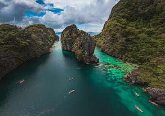 Tourists Kayaking Through the Turquoise Waters of Big Lagoon with impresive cliffs and bangka boats moored in a sunny day in Minoloc Island, El Nido, Palawan, Philippines