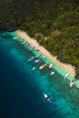 Aereal view of Colorful Bangka Boats Docked on the Crystal-Clear Waters and Coral Reefs of Entalula Island with a beautiful beach with people in El Nido, Palawan, Philippines