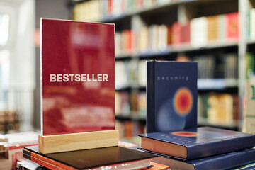 Stack of hardcover books displayed on table in bookstore foreground, prominent red sign reading...