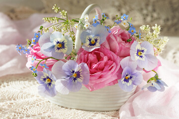 Bouquet of spring and summer flowers in a basket on the table, rose, pansies, forget me not flowers, beautiful postcard, still life, blur.