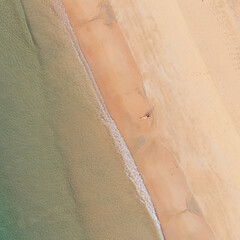 Bird's eye top aerial view of woman relaxing in sandy beach in the pristine turquoise shoreline and sweeping coastal landscape of Nacpan Beach in El Nido, Palawan, Philippines