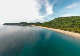 Stunning aerial view of Nacpan Beach’s winding shore, vibrant tropical greenery, and sparkling clear sea in El Nido, Palawan, Philippines