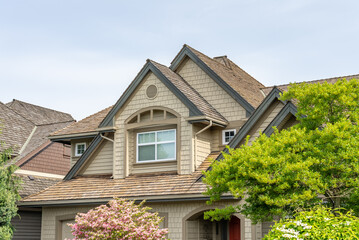 Top of grey stucco luxury house with shingle roof, green trees and nice windows in Spring in Vancouver, Canada, North America. Day time on May 2025.