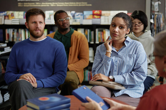 Diverse group of young adult and middle aged men and women listening attentively during session with author in bookstore, multiethnic audience focusing on speaker