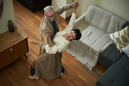 Elderly couple enjoying ballroom dance in warm living room with wooden floor and cozy furniture. They seem happy, embracing each other and smiling warmly while dancing - Powered by Adobe