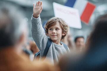 Excited young boy waves in a crowd, holding a backpack. He awaits arrival at an airport. Concept anticipation, reunion, welcome, travel. Travel, family, child.