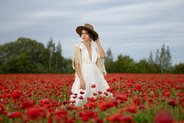 Young woman in a white dress and hat posing among summer poppies