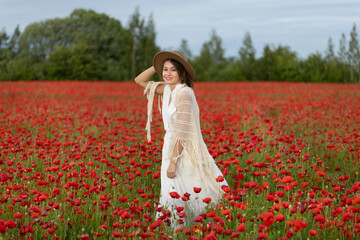 Young woman in a white dress and hat posing among summer poppies
