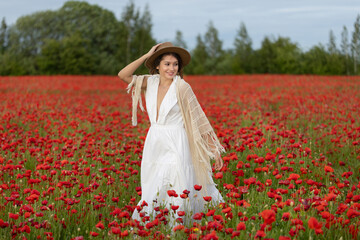 Young woman in a white dress and hat posing among summer poppies