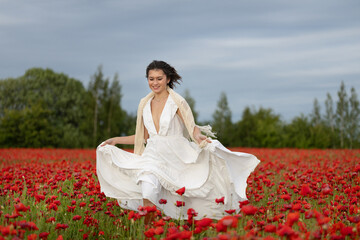 Happy young woman in a white dress runs through a summer poppy field