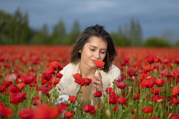 Young woman in a white dress smells the poppies in a summer field