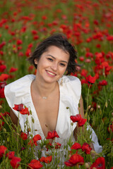 Young woman in a white dress posing among summer poppies