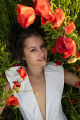 Young attractive woman lies among summer poppies, gazing at the camera