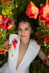 Young attractive woman lies among summer poppies, gazing at the camera