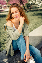 Beautiful young woman enjoying a sunny spring day outdoors, sitting relaxed in a park surrounded by...