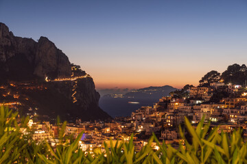 Sunset casts a warm glow over Capri Island, Italy highlighting charming buildings and the rocky cliffs, creating a serene atmosphere.