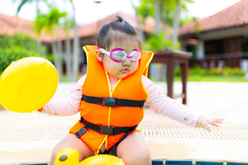 Cute little Asian girl wearing life jacket playing in swimming pool,Asian girl wearing life jacket...