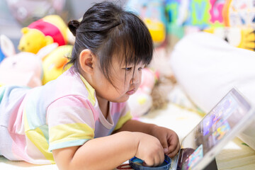 A little Asian girl is lying on the bed watching a tablet,Asian girl lying on bed in bedroom and...