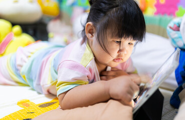 A little Asian girl is lying on the bed watching a tablet,Asian girl lying on bed in bedroom and...