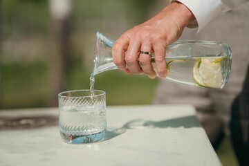 Closeup shot of a hand pours lemon water from a clear glass carafe into a textured tumbler