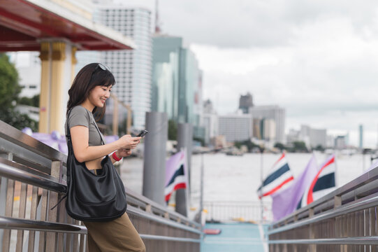 Happy young southeast asian woman searching map on smartphone tourism guide. World travel explorer enjoying local cultural experience in Bangkok Thailand by Chao Phraya river - Powered by Adobe