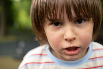 Angry little blonde kid boy 5 years old in the park. Awkward age, facial expression. Angry...