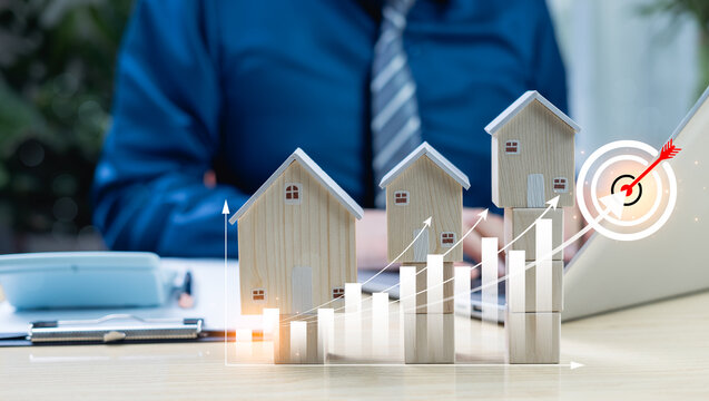 Real estate market growth with rising interest rates. Person writing on laptop with upward graph and house icons, symbolizing property investment and housing trends.