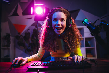 Excited female streamer gaming with colorful neon lighting in a modern home studio at night...
