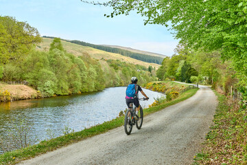active senior woman riding her electric mountain bike along the Caledonian Canal near Fort William...